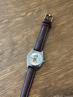 Photo of vintage Disney Mickey Mouse watch laid flat on a wooden surface showing face and leather band.