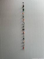 Full vertical view of the hanging wall decor showing the entire string of assorted gemstones and natural stones against a textured vertical panel background.