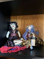 Two handmade vintage Martha Lewis dolls displayed on a shelf: one detailed female doll in dark dress, one elderly/wizard character doll with staff