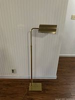 Full image showing the full height and design of the mid-century brass floor lamp with square base against wall and floor.