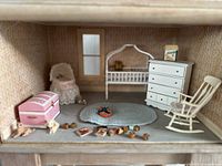 Full view showing the arrangement of the miniature furniture and accessories including rocking chair, dresser, cradle, pink chest, braided rug, and toys.