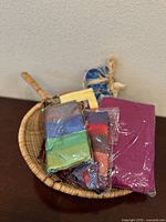 Full view of woven basket holding multiple colorful textile pieces, some packaged.