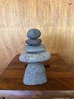 Front view of stacked stones sculpture showing five balanced stones of varying size and texture on a wooden surface with a plain wooden background.
