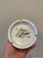 Close-up photo of the white porcelain ashtray showing the gold leaf design and 'The Fairmont Hotels' logo inside.