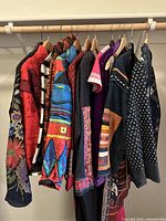 Full view of nine vintage women's clothing items hanging on a wooden rod, showing a variety of colorful patterned jackets and tops.