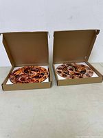 Two dragon design wall clocks in open cardboard boxes showing front faces with carved dragons and large black numbers, new in box condition.