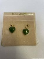 Front view of green jade heart-shaped earrings on display card labeled B.C JADE.