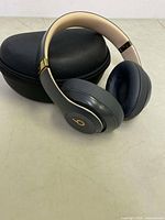 Beats Studio headphones resting on closed black hard case on a flat surface, showing earcups and headband with gold accent.