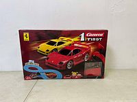 Front view of boxed Carrera 1 First slot car race track featuring Ferrari cars, showing yellow and red Ferrari cars on the track and the controllers.