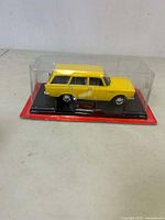 Side view of yellow Moskvich 2137 diecast model in clear plastic display case with red base.