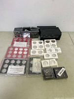 Overall lot of coin display and storage cases with black plastic boxes, white cardboard holders, and red and black display frames
