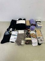 Photo showing multiple pairs of new socks including black, white, and patterned varieties laid out flat on the floor.