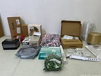 Wide shot showing all miscellaneous items including boxes, textile, plastic plant, and electronic device on floor.