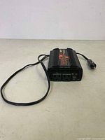 Top-down view of MotoMaster Eliminator 400W power inverter showing black rectangular form, top branding label, and attached 12V cigarette lighter plug cable.