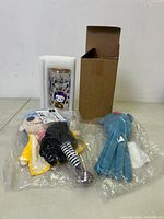Two plush dolls sealed in plastic bags next to a boxed glass drinking glass with foam packaging