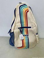 Front view of cream colored Pickle bag with rainbow stripes and front zippered pocket, showing attached new retail tag.