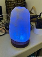 Salt lamp glowing blue on a wooden base with power cable visible.