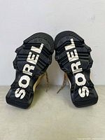 Bottom view of both boots showing large 'SOREL' branding on black rugged tread sole with star_patterns