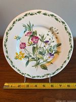 Front view of the salad plate showing colorful floral pattern and green leaf border around rim with 8-inch measurement taped in front.