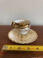 Front view of demitasse cup on saucer with measuring tape showing cup height approx 2.25 inches and saucer width just under 4 inches.