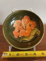 Front view of Moorcroft bowl showing orange hibiscus flower design inside on green background with measuring tape showing about 5 inches diameter