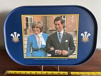 Blue serving tray with image of Prince Charles and Lady Diana Spencer, with wedding date July 29, 1981, showing a ruler for scale.