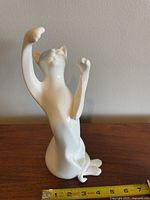Front view of white porcelain Royal Doulton cat figurine posed with front paws raised, sitting on a wooden surface with a measuring tape showing approximately 10.5 inches tall.