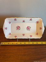 Front view of rectangular bone china tray showing Tudor Rose floral pattern with pink roses and green leaves and gold detail on scalloped edges, placed on a wooden surface with measuring tape showing approximately 11 inches length.