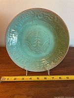 Front view of turquoise glazed pottery plate with embossed indigenous patterns and tree motif