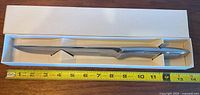 Top view of the carving knife in its original white box next to a tape measure showing the knife is about 13.5 inches long