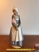 Front view of the Nao girl figurine standing on a wooden surface with a tape measure for scale, showing height around 15 inches.