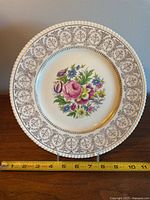 Front view of the 11-inch Ambassador Athlone ceramic plate showing floral pattern and decorative border with gold accents, placed next to measuring tape.