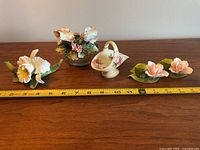 Wide view of all four porcelain floral decor items on wooden surface with measuring tape for scale, showing size and condition