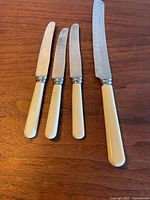 Four knives pictured with ivory handles, three small butter knives and one large serrated Granton knife.