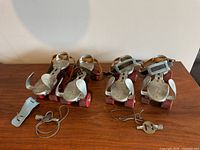 Two pairs of vintage metal roller skates with red wheels and leather straps, placed side by side on wood surface with keys shown separately