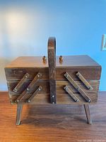 Closed view of the vintage wooden sewing chest showing solid wood exterior, accordion hinge mechanics, and top handle.