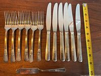 Full set of 6 forks, 6 knives, and 1 butter knife arranged on wooden surface with measuring tape for scale.