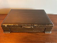 Closed wooden box with visible wear and paint scratches on the edges, dark brown finish.