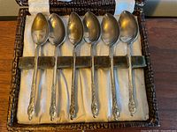 Six silver plated teaspoons with ornate handles in a lined box, showing front detail and condition.