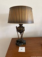 Full lamp view showing bronze sculpture stand with cherubs and black marble base, topped with a black and gold striped lampshade.