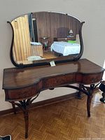 Front view of antique wooden vanity table with large attached movable mirror and three drawers.