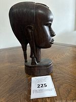 Side profile of dark brown wooden bust head showing hair braids and facial profile