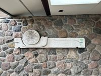 Full view of the concrete art panel mounted on a stone wall, showing the entire length with the circular patterned element on the left side.
