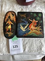 Two lacquer boxes on a white cloth, showing their painted tops with Russian folklore art.