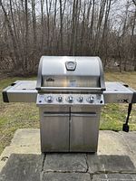 Front view of closed grill showing stainless steel lid, built-in gauge, four main control knobs and fold-out side shelves