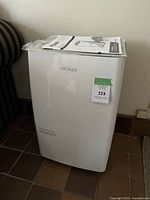 White NOMA dehumidifier with instruction manual placed on top, viewed from the front.