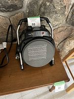 Front view of Valymo portable electric heater placed on wooden table against stone wall background, showing metal grill and control panel.