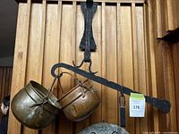 Front view of the hanging scale showing ironwork, two brass pots, and hanging weight.