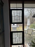 Two green-framed stained glass panels hanging vertically in window with outdoor view behind