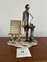 Front view of bisque porcelain teacher figurine showing detailed hand painting, glasses, blackboard, and presence of signage with letters and numbers.